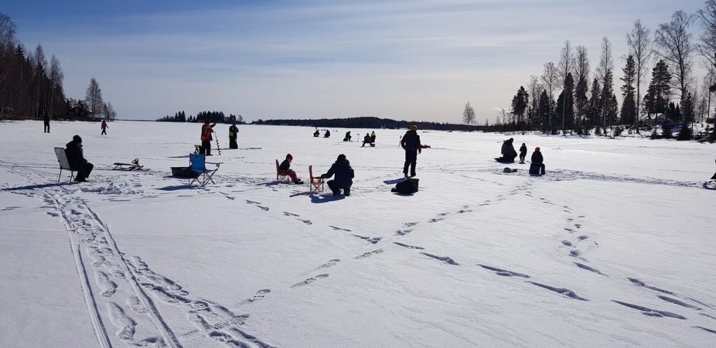 Flertalet välklädda människor på isen i timmerviken under Örvikens årliga pimpeltävling